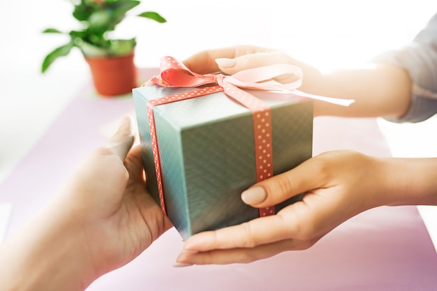 Close-up of female hands holding a present. trendy pink desk.