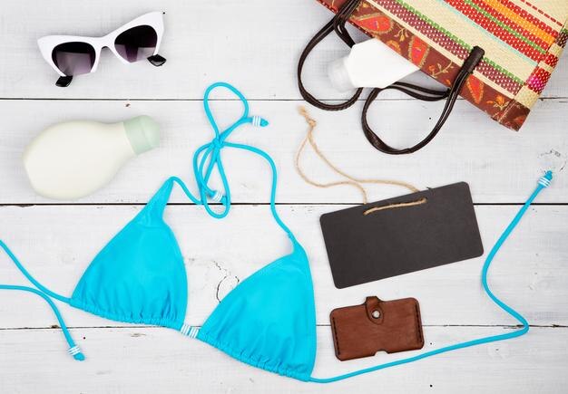 Summer women's fashion with blue swimsuit straw bag chalkboard sunglasses and sunscreen